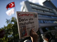 Протестующий с выпуском Cumhuriyet рядом с офисом редакции газеты в Стамбуле, заголовок на первой полосе: «Новый рейд против оппозиции»